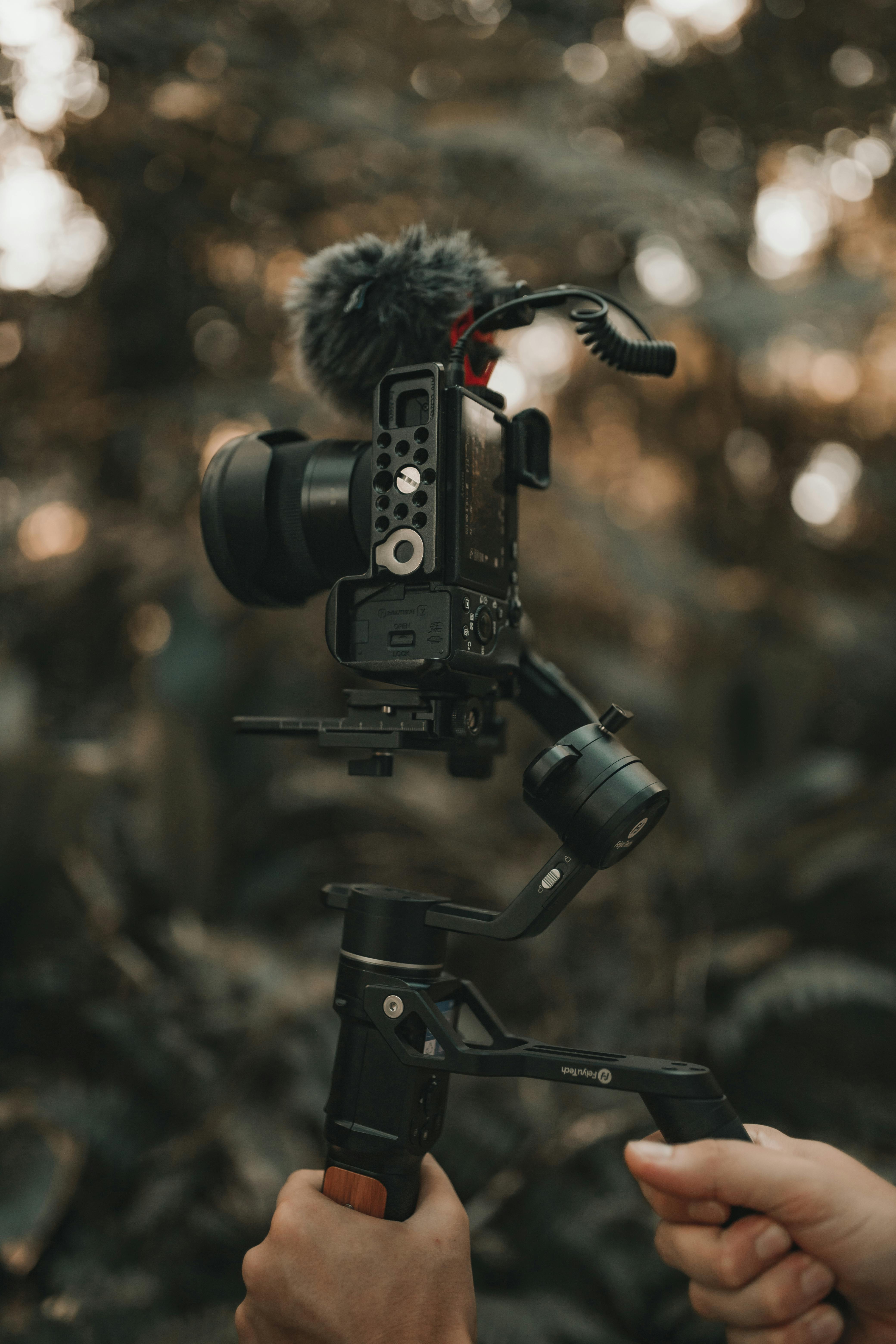 Hands holding a camera on a gimbal in an outdoor setting with blurred background.